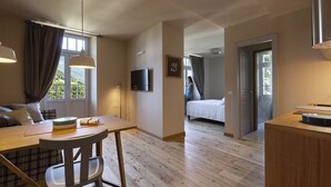 A modern, well-lit room with a wooden dining table, a sofa, and a bed. A television is mounted on the wall, and there is a window with curtains. - QC Terme Panoramic Apartament (Valdidentro)