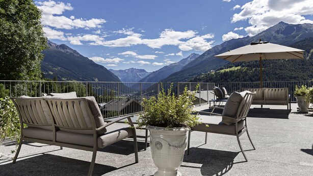 A terrace with outdoor seating and a potted plant, overlooking a mountainous landscape. - QC Terme Panoramic Apartament (Valdidentro)