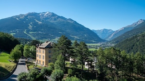 A mountain lodge with a prominent building in the foreground, surrounded by lush greenery and a valley with a distant mountain range. - QC Terme Panoramic Apartament (Valdidentro)