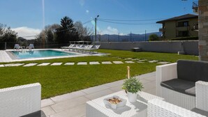 A sunny outdoor area with a swimming pool, lounge chairs, and a covered patio with white wicker furniture. - Villa Il Gelsomino Bellavista (Besozzo)