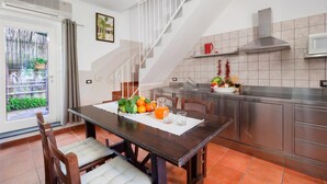 A modern kitchen with a dining area, featuring a staircase, a window with a view of greenery, and a kitchen island with fresh produce. - Residence Limoneto - Casa Limoneto (Sorrento)
