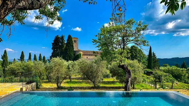 Ein Pool mit Blick auf ein historisches Gebäude und umliegende Bäume.