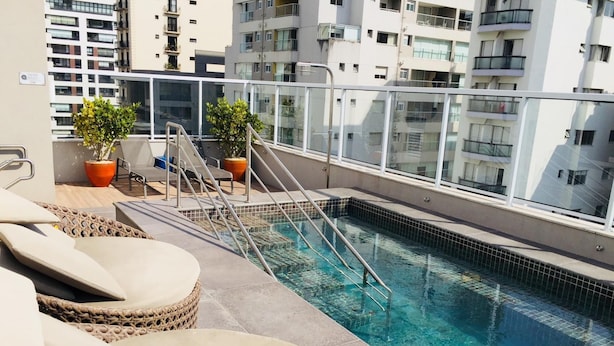 Una piscina en la azotea con sillones de descanso, plantas en macetas y vistas de edificios circundantes.