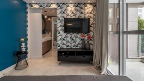 Una sala de estar moderna con un televisor montado en una pared con diseño geométrico, un mueble de entretenimiento negro y vistas al exterior a través de un ventanal grande.