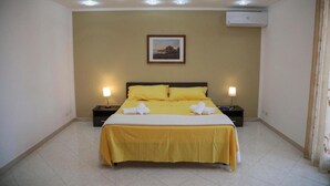 A hotel room with a bed, two bedside tables, a wall-mounted air conditioner, and a framed picture above the bed. - Seascape Terrace Spacious Apartment With Terrace (Cefalù)