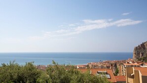 A coastal town with terracotta-roofed buildings, a clear sky, and the sea in the background. - Seascape Terrace Spacious Apartment With Terrace (Cefalù)