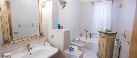Een badkamer met een grote spiegel, twee wastafels, een badkuip en een radiator.