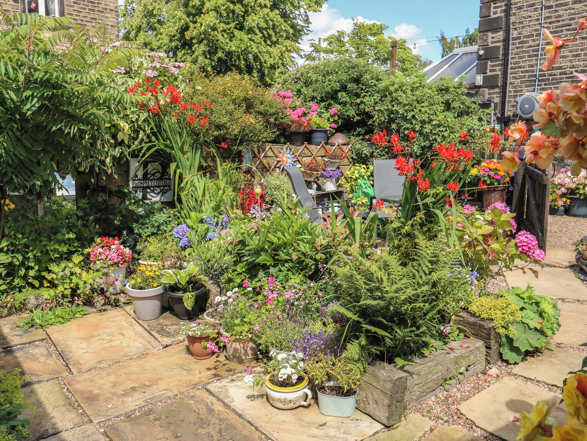 Un jardin agrémenté de diverses plantes et fleurs en pot, de chemins en pierre et d’une clôture en bois.