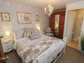 A bedroom with a bed, nightstands, a chair, a chandelier, and framed pictures on the wall. - Prospect Cottage (Sowerby Bridge)