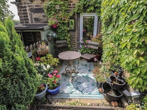 A small courtyard with a round table and benches, surrounded by potted plants and a variety of flowers. - Prospect Cottage (Sowerby Bridge)