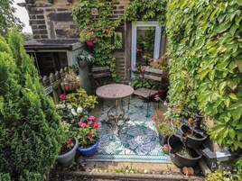 A small courtyard with a round table and benches, surrounded by potted plants and a variety of flowers.