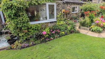 Una casa in pietra con giardino, prato e una finestra.