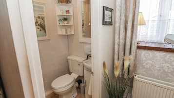 Baño pequeño y funcional con inodoro, lavabo y espejo. Objetos decorativos adornan la pared y hay una ventana con cortinas.