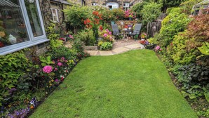A well-maintained garden with a lawn, various flowering plants, and a seating area with chairs and a table. - Prospect Cottage (Sowerby Bridge)