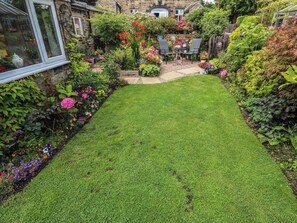 A well-maintained garden with a lawn, various flowering plants, and a seating area with chairs and a table. - Prospect Cottage (Sowerby Bridge)
