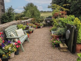 Un patio jardín con un sendero de grava, una valla de madera y diversas plantas en macetas.