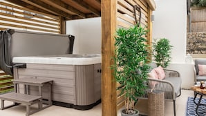 A covered outdoor area with a hot tub, seating, and potted plants. - Driftwood (Newquay)