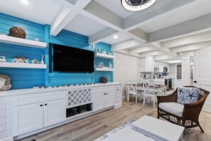 Una sala de estar moderna con un televisor de pantalla plana grande, muebles blancos y una pared de acento azul.