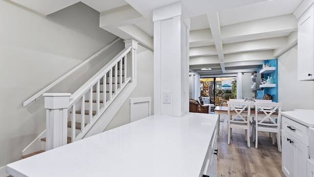 A modern kitchen with white cabinetry, a central island, and a staircase with white railings. - Beautiful remodeled Condo w/ Pool  Walk to Beach, Coligny, Celebration Park ! (Hilton Head Island)