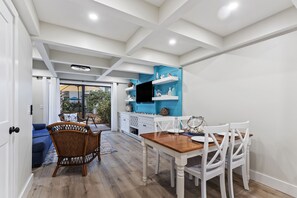 Un comedor con una mesa de madera y sillas blancas, una pared azul decorativa y una cocina con armarios blancos y estantes azules.