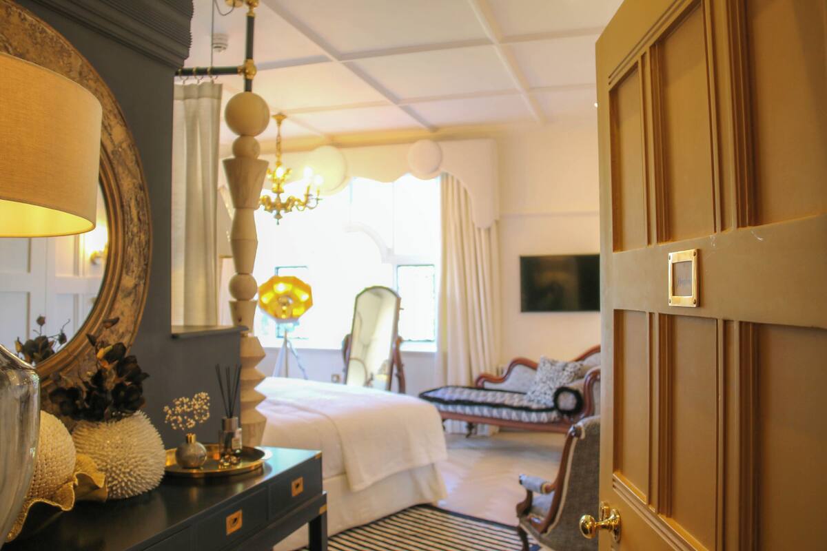 A room with a bed, a dresser, a mirror, a chandelier, and a door.