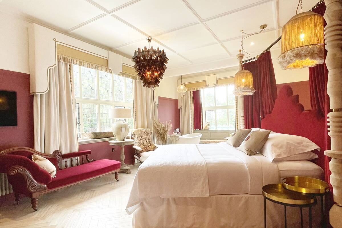 A spacious bedroom with a large bed, a sitting area with a sofa, and a view of the outdoors through the windows.