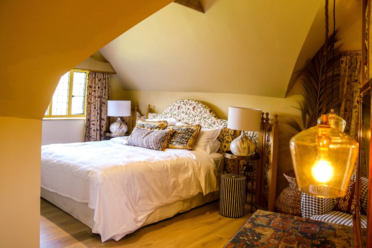 A bedroom with a large bed, a nightstand, a lamp, and a decorative vase.