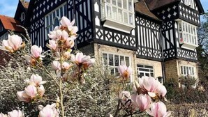 Un edificio de estilo Tudor con una fachada simétrica, numerosas ventanas y una entrada destacada.