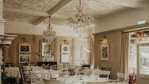 Un comedor formal con techo ornamentado y candelabros, mobiliario blanco y obras de arte enmarcadas en las paredes.
