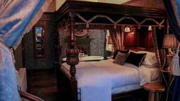A four-poster bed with a canopy, a bedside table, a mirror, and a nightstand with a lamp.