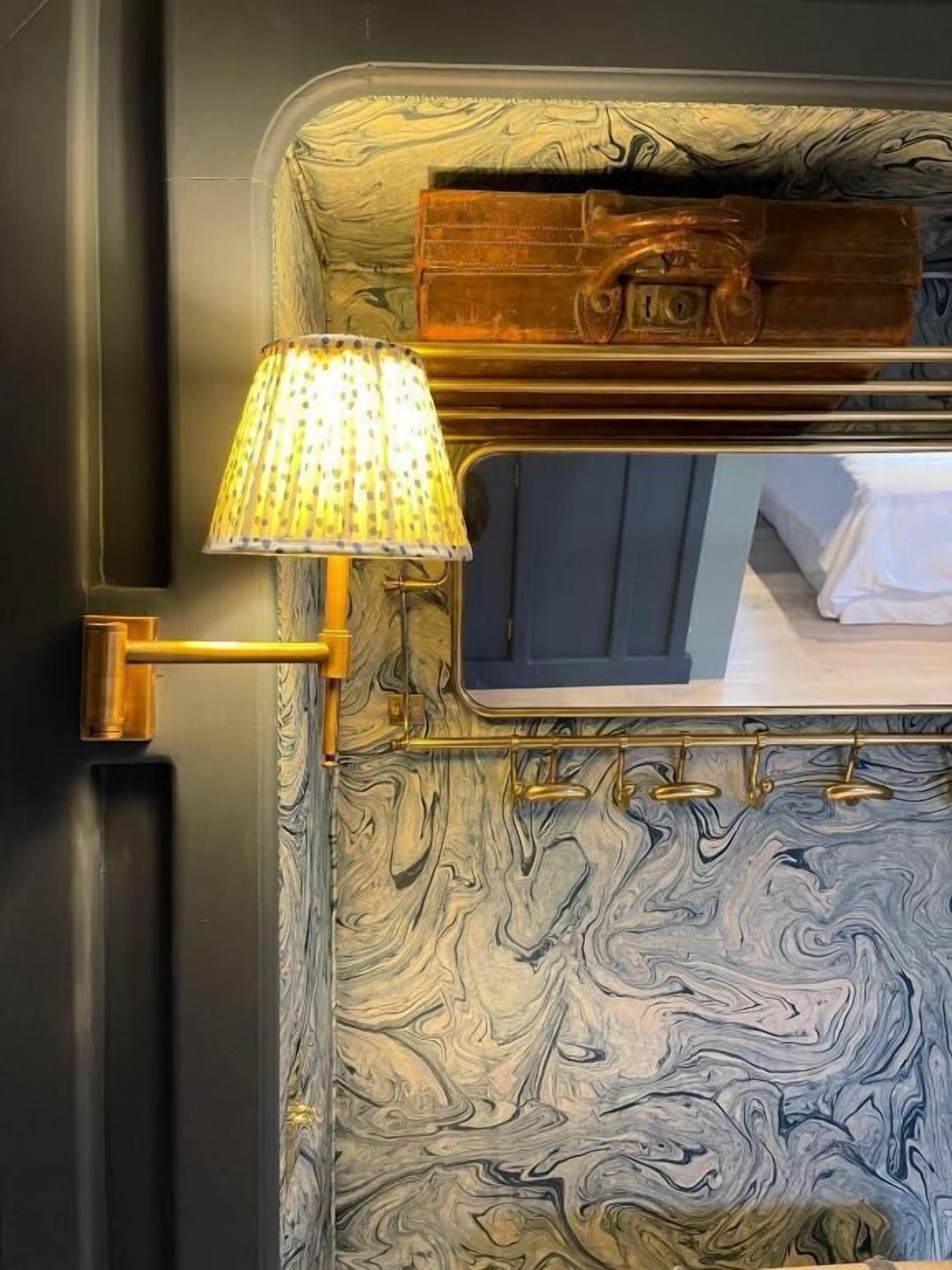 Een badkamer met een marmeren wand, een spiegel met gouden lijst en een lamp met een behangetje.