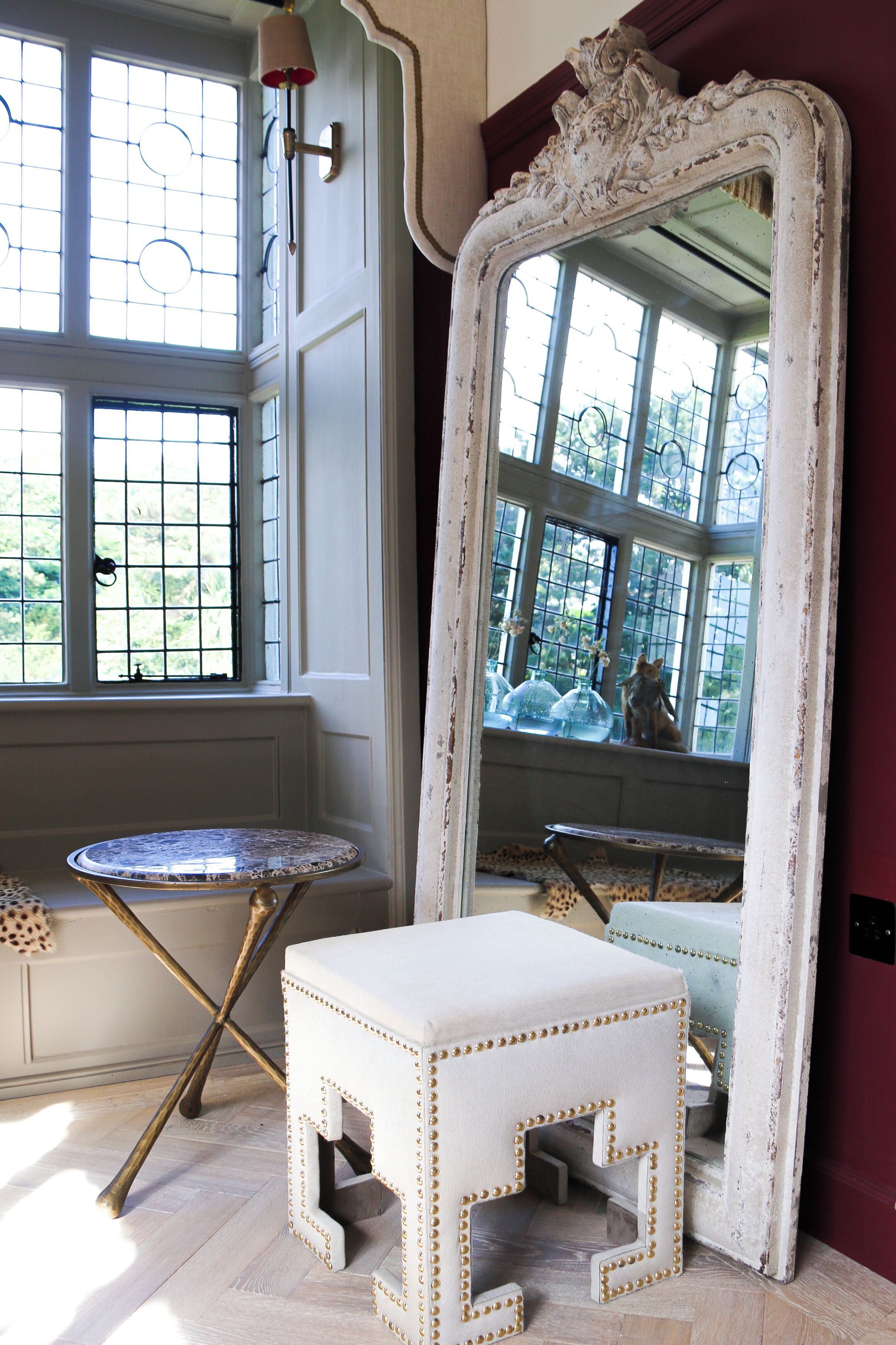 A room with a large ornate mirror, a small round table, and a stool with decorative studs.