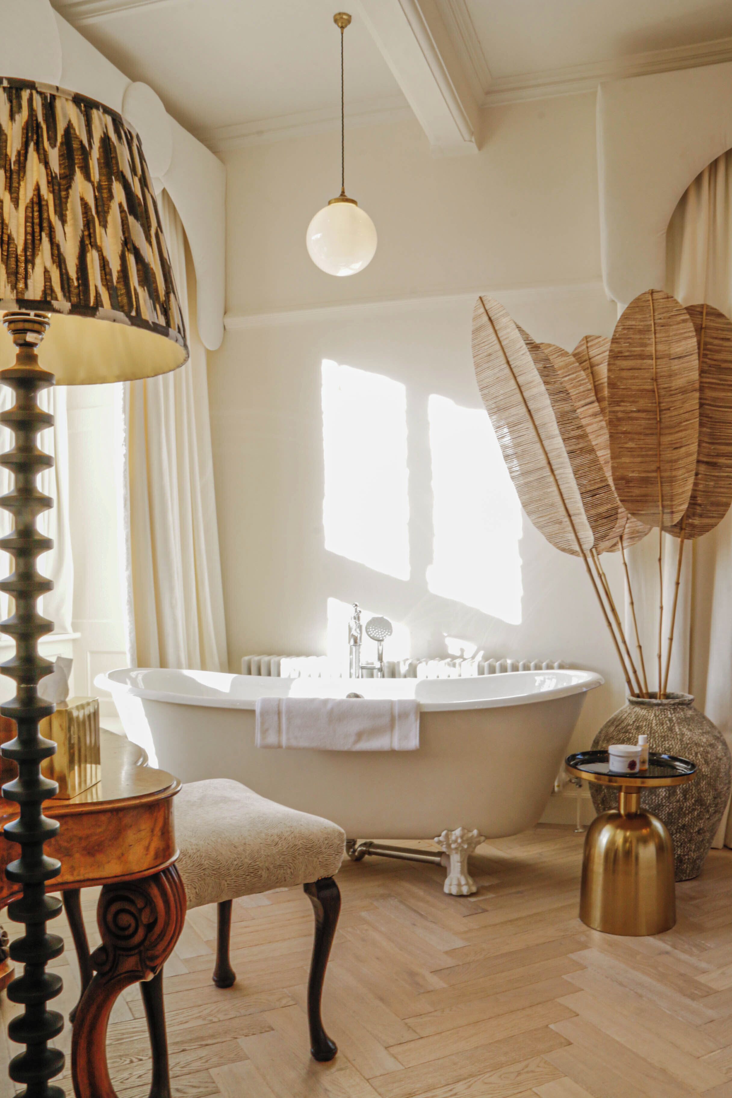 A bathroom with a freestanding bathtub, a vanity with a mirror, a towel, and a decorative vase with dried reeds.