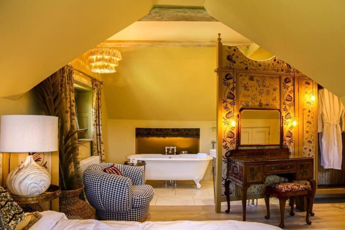 A bedroom with a large bed, a vanity with a mirror, a bathtub, and a chandelier.