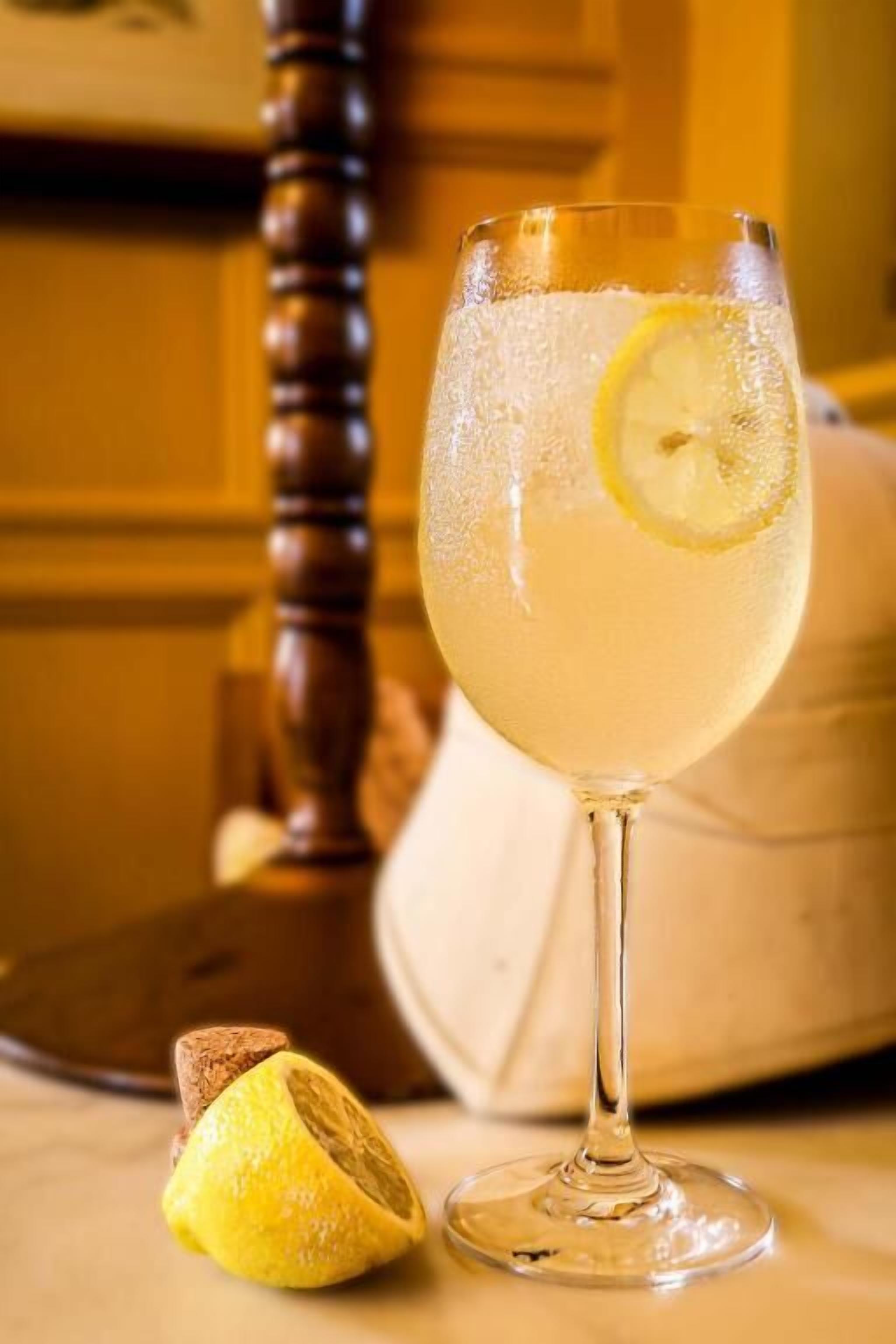 A glass of clear beverage with a lemon slice, a cork, and a wooden object in the background.