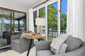 A modern living room with a grey sofa, a round wooden table with a chess set, and a lamp.