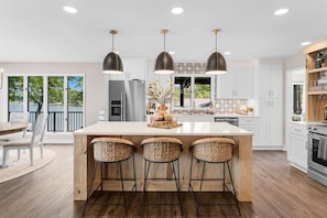 A modern kitchen with a central island, pendant lights, and a view of the outdoors. - Whiskey Sunsets: Stunning Peninsula Retreat with Panoramic Lake Views, Dock, Hot Tub, and More! (Mooresville)