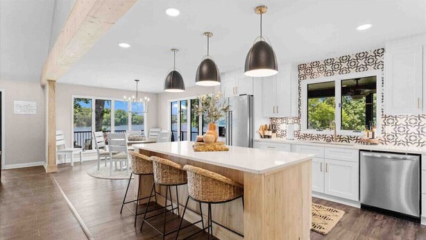 Una cocina moderna con una isla grande, taburetes de bar, iluminación colgante y vistas al exterior.