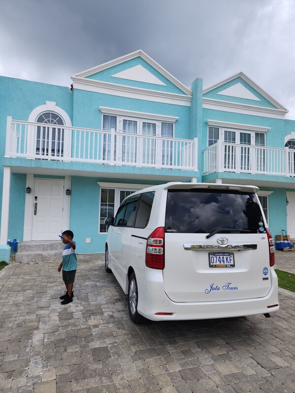 A white minivan parked in front of a two-story building with a balcony.