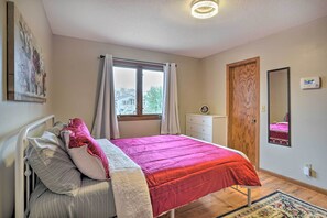 Um quarto com cama, janela com cortinas, cômoda, espelho e termostato na parede.