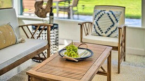 Un rincón acogedor con una mesa de madera, una silla de mimbre y un sofá. En la mesa, una bandeja con uvas verdes y un libro.