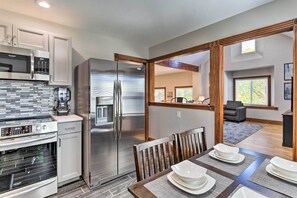 A modern kitchen with stainless steel appliances, a dining area with a wooden table and chairs, and a view into the living room. - Deck + Fenced Yard: Capitol Hill Townhome (Denver)