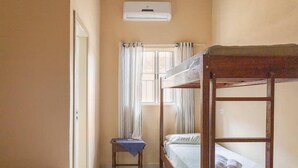 A bedroom with a bunk bed, a bedside table with a lamp, and a window with curtains. - Casinha da Vila (Ilhabela)