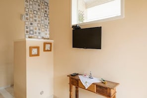 A room with a TV mounted on the wall, a small wooden table with a cloth, and a tiled wall above the table.