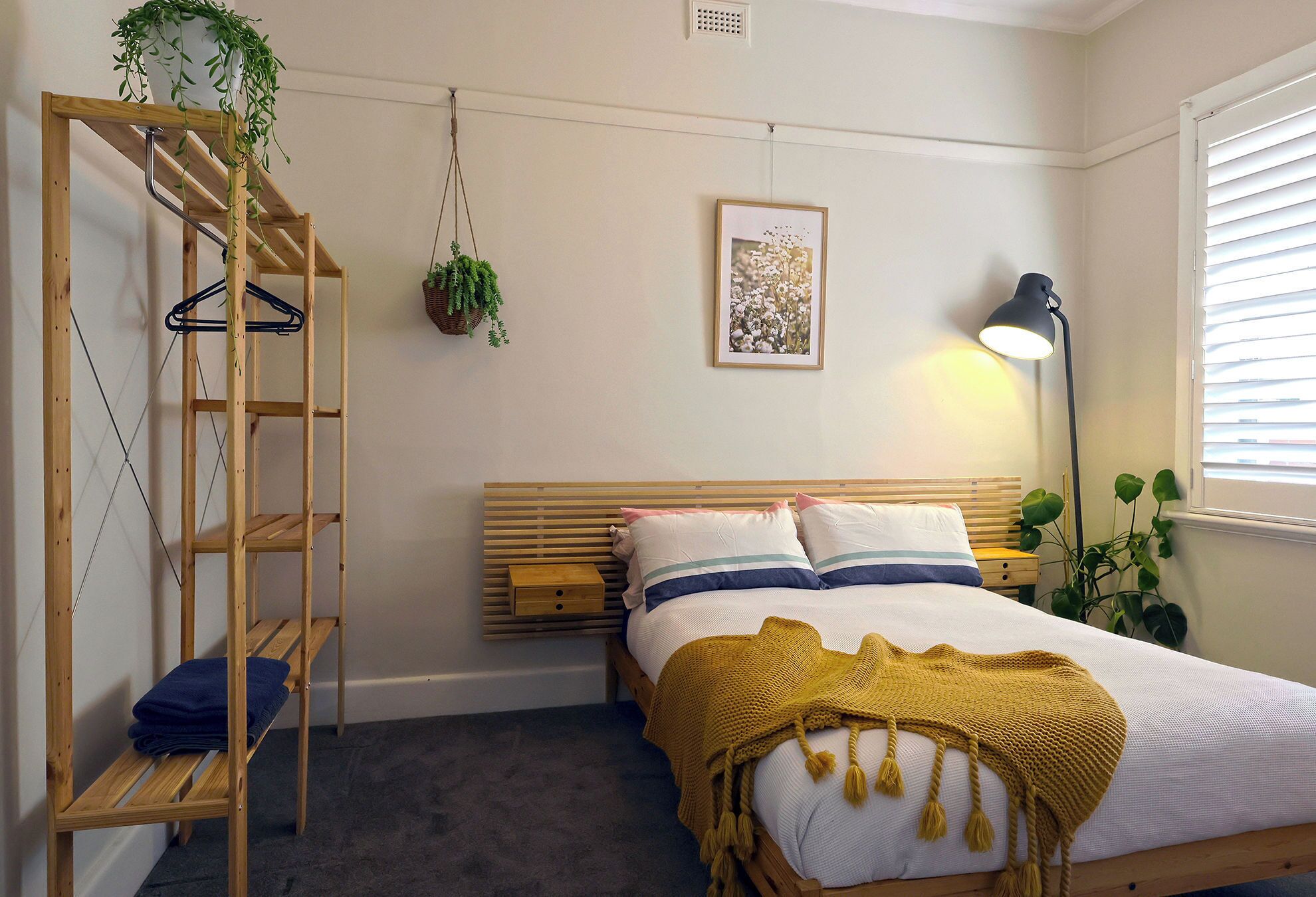 A bedroom with a bed, a wooden ladder, a hanging plant, a framed picture, and a bedside lamp.
