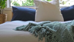 Una cama con un plaid verde de punto, una almohada blanca y una almohada azul oscuro.