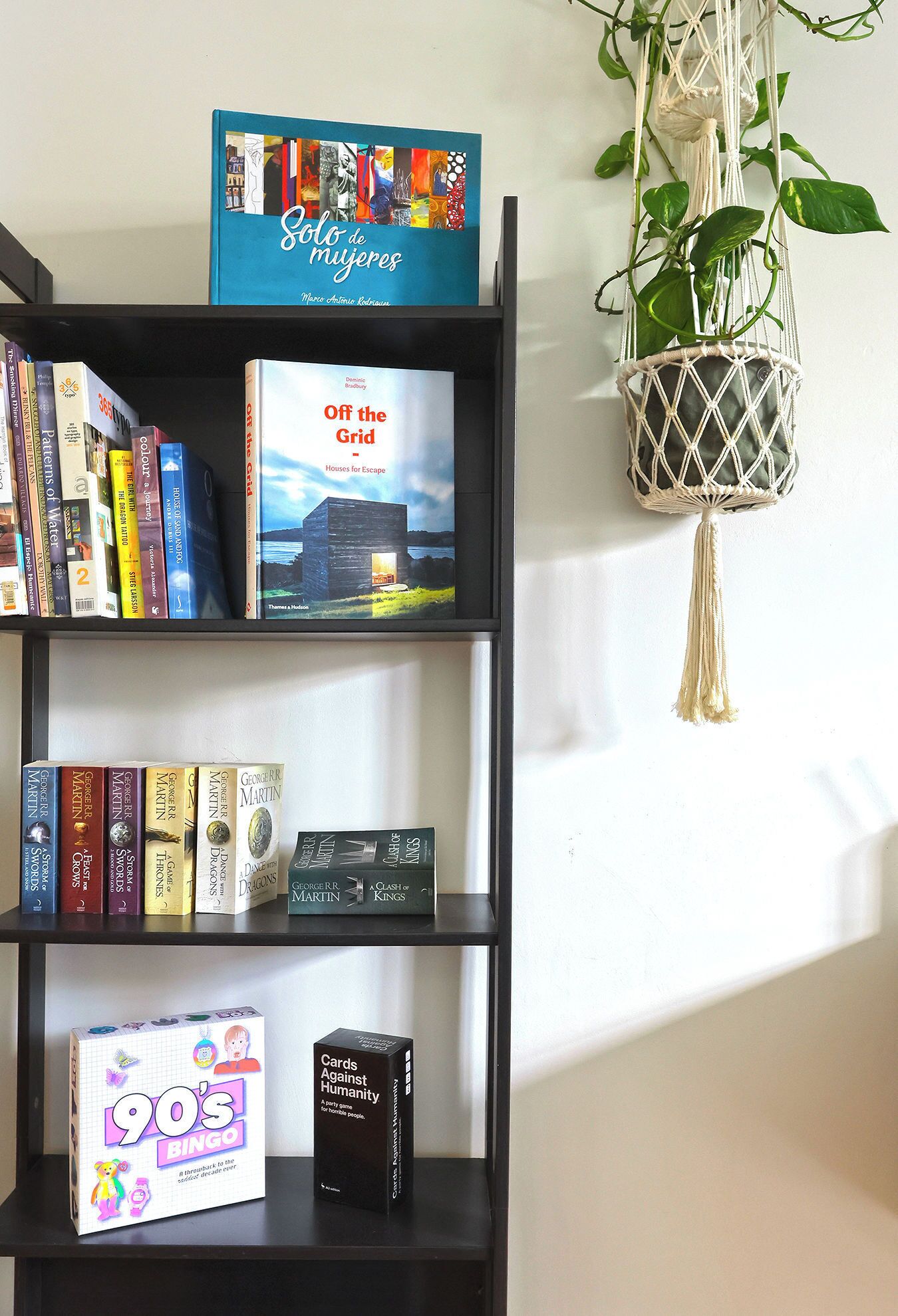 A bookshelf with books, a board game, and a plant.