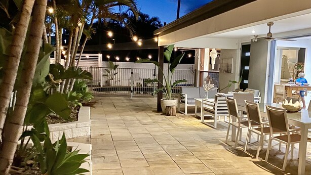 Un'area patio esterna con pavimento in pietra, mobili bianchi e luci a stringa.