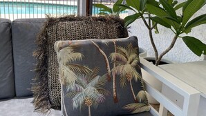 Zona relax esterna moderna con vista piscina, con un divano con cuscini decorati e un’ampia pianta in vaso.
