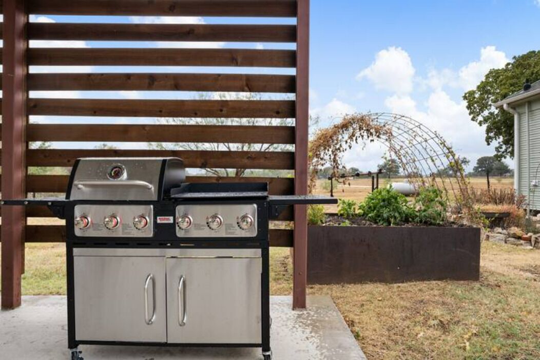 An outdoor grill setup under a wooden pergola.